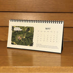 Calendar with a glass frog illustration on a wooden surface