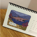 Calendar page with illustration of a goblin shark on a wooden surface