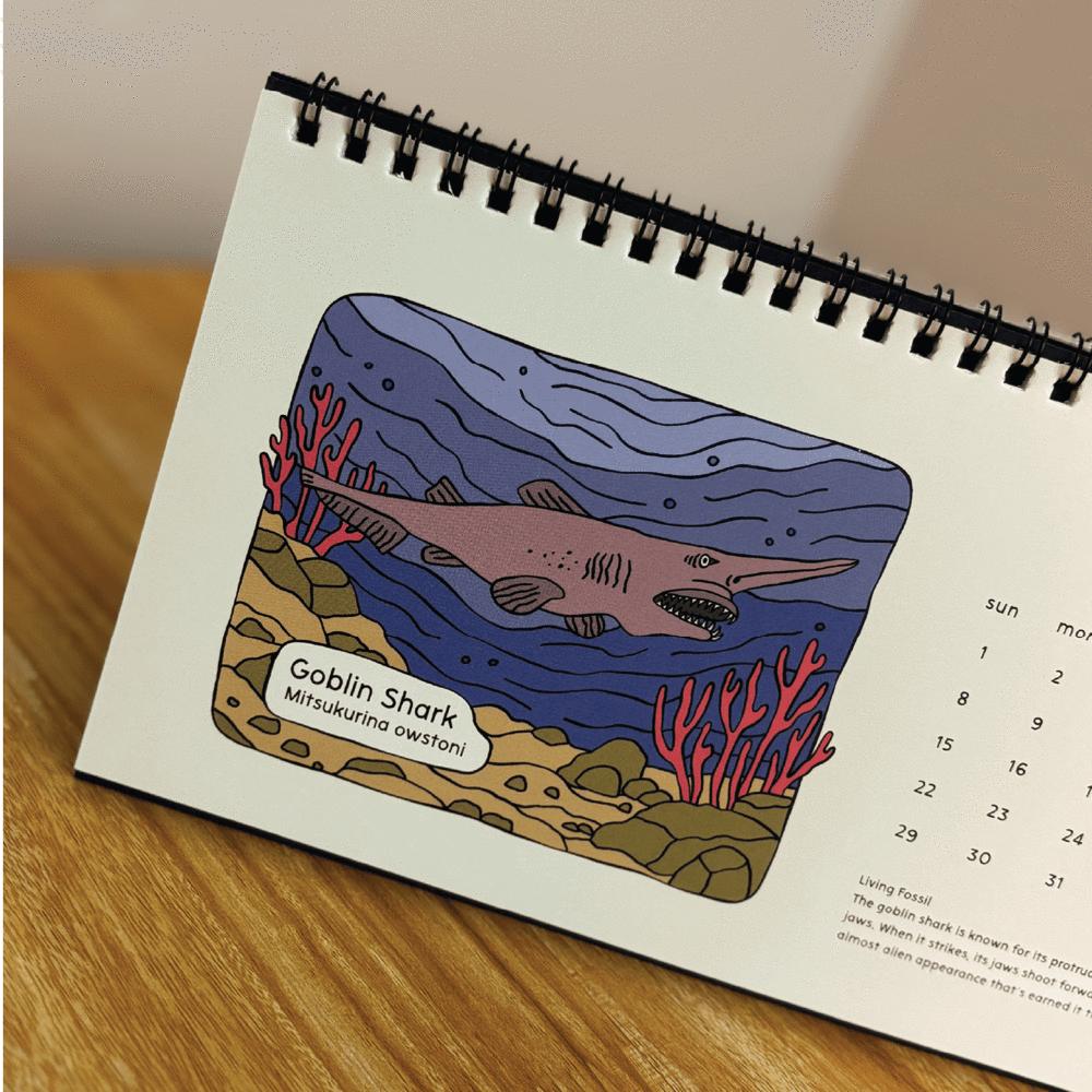 Calendar page with illustration of a goblin shark on a wooden surface