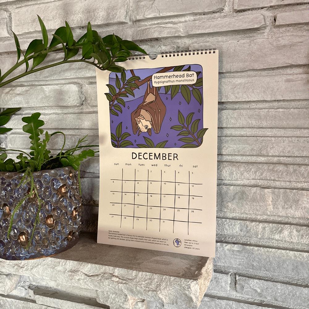Calendar with a December layout and a hammerhead bat hand drawn illustration on a stone surface next to a plant and toys